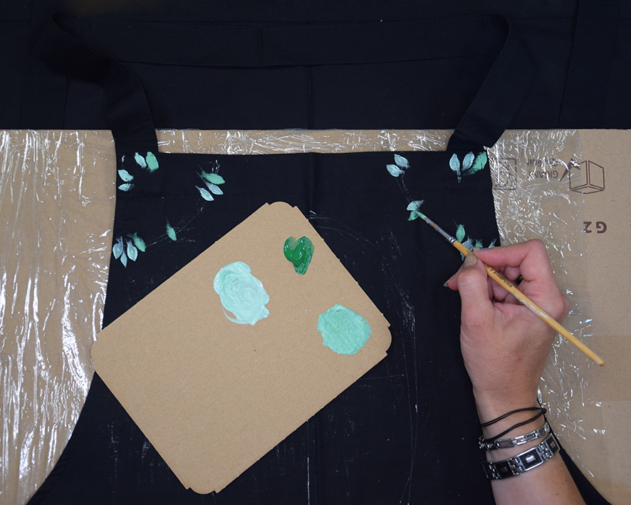 Žena pomocou ledších odtieňov zelenej farby na textil maľuje listy od najbledších po najtmavšie.